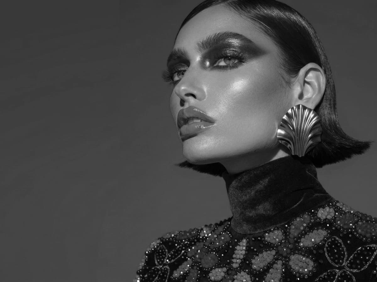 Portrait of a model in a beaded floral top and a gold shell earring, rendered in black and white.